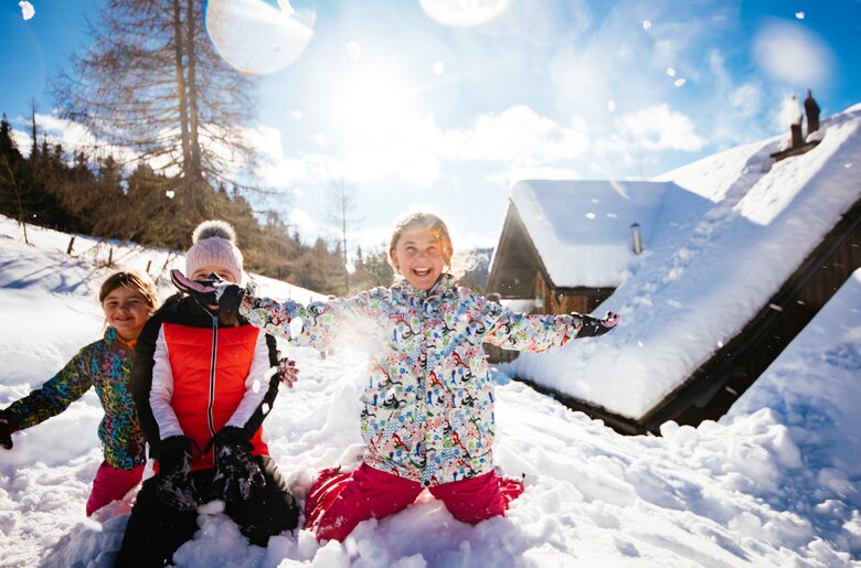 Kinder im Schnee lachen und werfen mit Schneebällen auf der Almhütte  | © Urlaub am Bauernhof Kärnten / Daniel Gollner