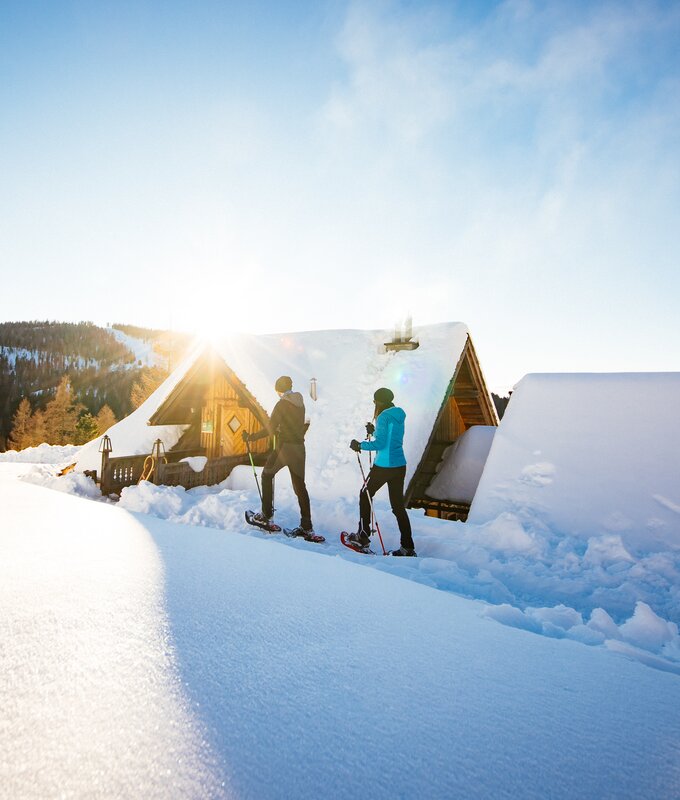 Zwei Schneewanderer in Aktion, vor malerischer Berglandschaft mit Hütten, bei Sonneneinstrahlung und Winterszenerie. | © Urlaub am Bauernhof Kärnten / Daniel Gollner