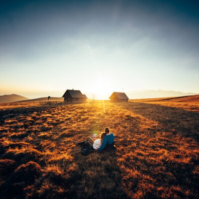 Paar sitzt vor der Hütte im Gras und genießt den Sonnenuntergang auf der Alm | © Urlaub am Bauernhof Kärnten/ Daniel Gollner 