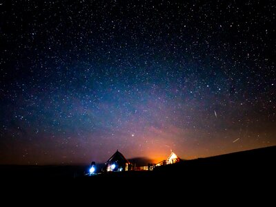 Sternenhimmel auf der Alm in Kärnten | © Urlaub am Bauernhof Kärnten/ Daniel Gollner Illuminated cabins nestled amidst a starry night sky, mountains silhouetted against the warm glow of lights. | © Urlaub am Bauernhof Kärnten/ Daniel Gollner