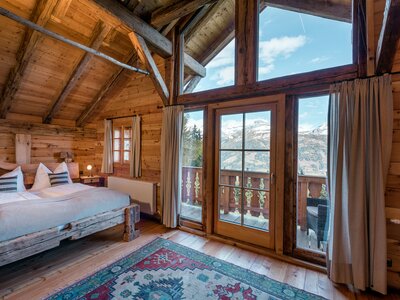 Premiumhütte Schlafzimmer | © Günter Standl Geräumiges Holzchalet mit hohen Decken, großen Fenstern und Balkon mit Blick auf Berge. Gemütliche Einrichtung mit dekorativen Kissen, Teppich und rustikalen Möbeln. Einladende Atmosphäre für einen Entspannungsurlaub in den Bergen. | © Günter Standl