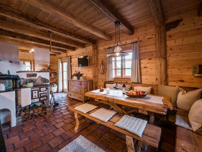 Blick ins Bergchalet Moseralm | © Günter Standl Gemütliches Holzinterieur mit rustikalem Esszimmertisch, einem Kaminofen und einer offenen Küche. Dekorative Details, wie Blumen und Naturalien, verleihen dem Raum eine charmante Atmosphäre. | © Günter Standl