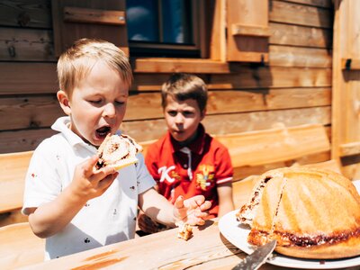 Ein Kind isst einen Kärntner Reindling vor der Almhütte im Sommer | © Urlaub am Bauernhof Kärnten / Daniel Gollner