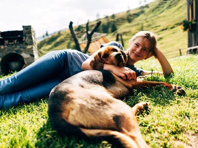 Mädchen und Hund in der Wiese | © Urlaub am Bauernhof Kärnten / Daniel Gollner Cheerful woman cuddles with friendly dog on idyllic grassy slope near rustic wooden structures. | © Urlaub am Bauernhof Kärnten / Daniel Gollner