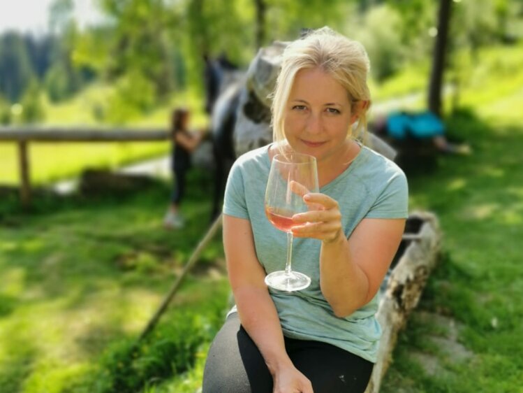 Eine Frau genießt einen Drink in einer ländlichen Umgebung mit Bäumen und Wiesen im Hintergrund. | © Urlaub am Bauernhof / Schell