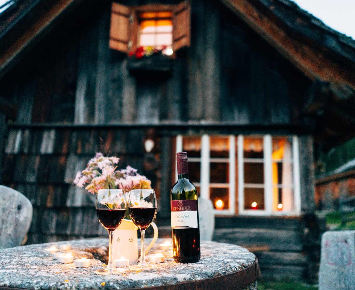 Romantischer Abend vor der Almhütte | © Urlaub am Bauernhof Kärnten/ Daniel Gollner zwei Rotweingläser stehen auf einem Tisch im Kerzenschein vor der Almhütte in Kärnten | © Urlaub am Bauernhof Kärnten/ Daniel Gollner