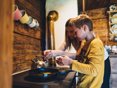 Ein Junge und ein Mädchen bereiten gemeinsam Essen in einer rustikal eingerichteten Küche zu. Sie stehen vor einer Kochplatte und scheinen konzentriert bei der Sache zu sein. | © Urlaub am Bauernhof Salzburg / Daniel Gollner 