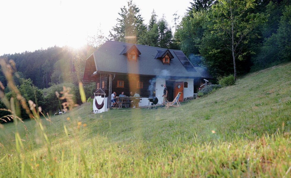 Auf einer idyllischen Almhütte umgeben von Wiesen und Wäldern wird gemeinsam gegrillt. Freunde sitzen auf der Veranda zusammen und reden. | © Urlaub am Bauernhof / Daniel Gollner