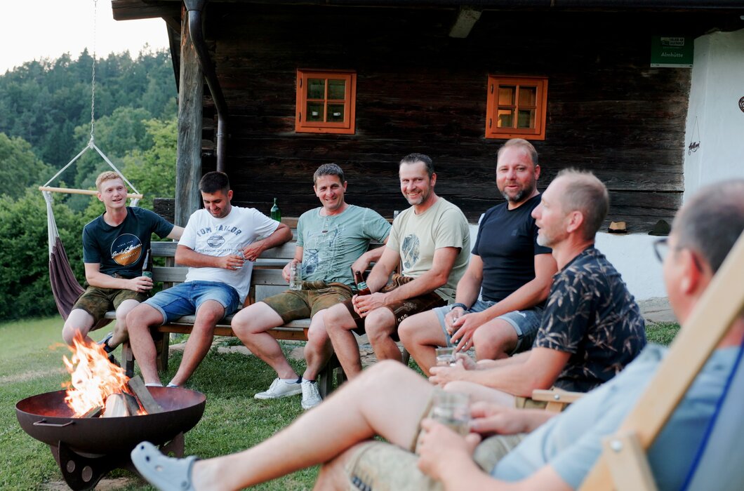 Freunde sitzen rund um ein knisterndes Lagerfeuer, lachen gemeinsam, reden miteinander und genießen ausgelassen die Abendstimmung. | © Urlaub am Bauernhof / Daniel Gollner