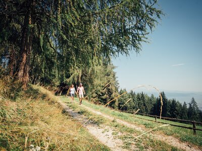 Zweisamkeit beim Urlaub auf der Alm in der Steiermark | © Urlaub am Bauernhof Steiermark / Daniel Gollner Two hikers strolling on a scenic mountain trail surrounded by lush, evergreen forests and clear blue skies. | © Urlaub am Bauernhof Steiermark / Daniel Gollner