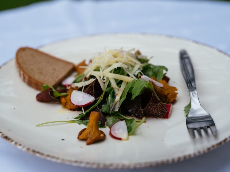 Auf einem weißen Teller liegt ein frisches Brot mit Eierschwammerl, Radieschen, Salat und Parmesan. | © Urlaub am Bauernhof Kärnten/ Angelina Tschische