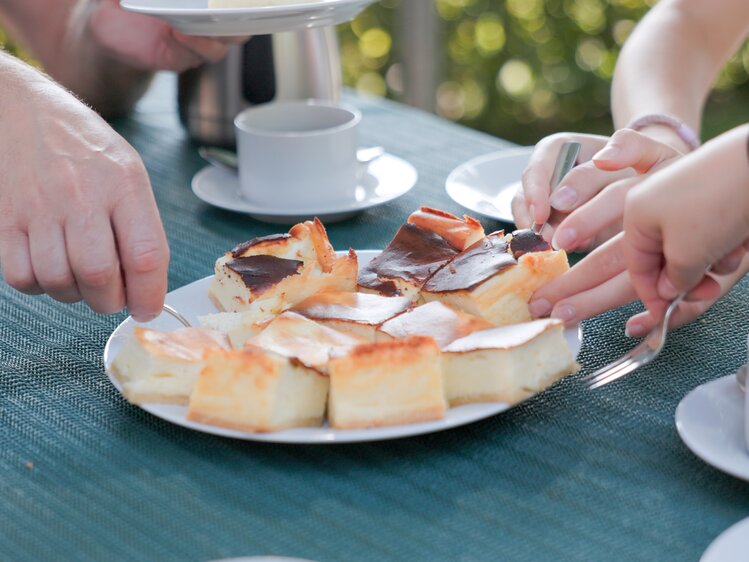 Menschen teilen ein Dessert mit verschiedenen Kuchenstücken auf einem Tisch im Freien.