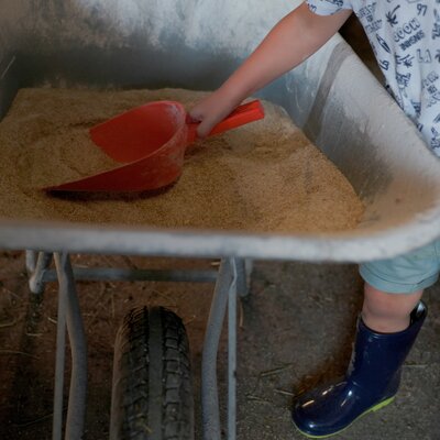 Ein Kind schaufelt Sand in einen roten Schieber in einem Garten oder auf einer Baustelle.
