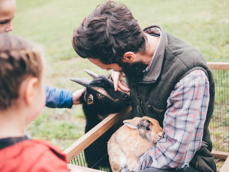 Mann und Kinder sind bei der Ziege und beim Hasen | © Urlaub am Bauernhof Kärnten / Daniel Gollner