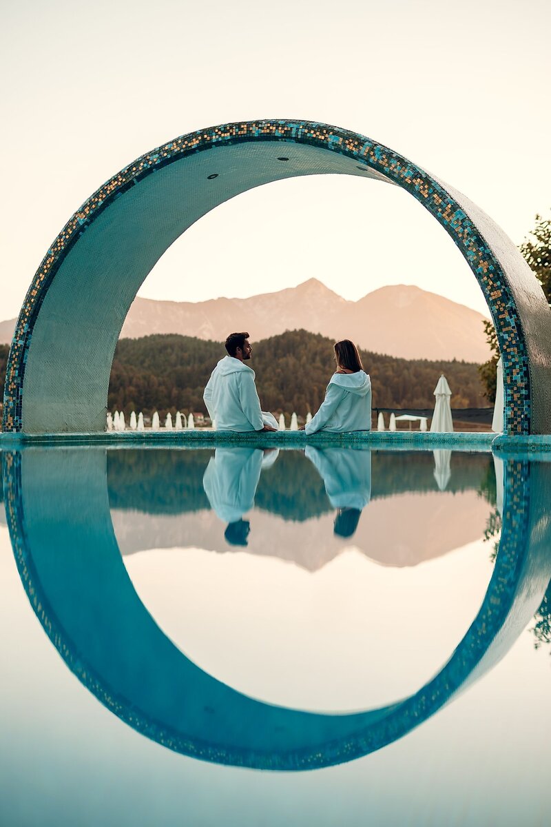 Paar sitzt am Rand des Pools im Hintergrund See und Landschaft | © Tourismusregion Klopeiner See - Südkärnten GmbH / Martin Hofmann