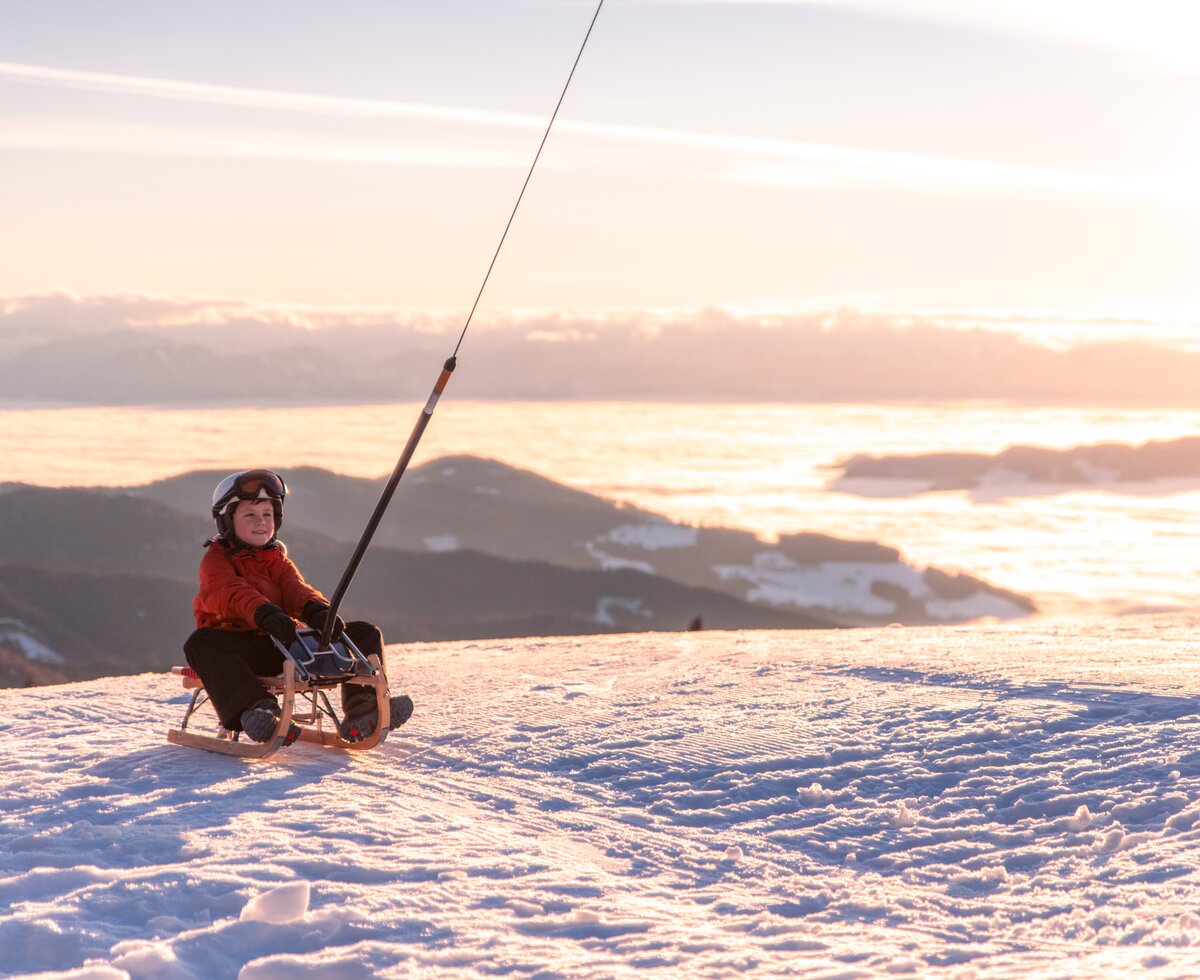 Winterspaß auf der Saualpe | © Michael Stabentheiner / Tourismusregion Mittelkärnten Kind auf Schlitten im Abendlicht im Schnee | © Michael Stabentheiner / Tourismusregion Mittelkärnten