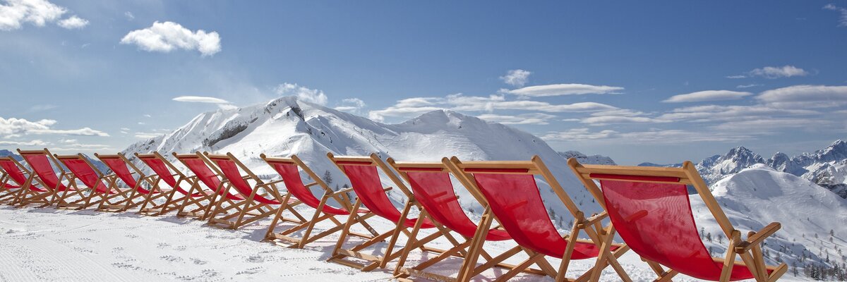 Liegestühle aufgereiht in der Sonne im Hintergrund das Skigebiet Nassfeld | © Martin Steinthaler - Kärnten Werbung GmbH