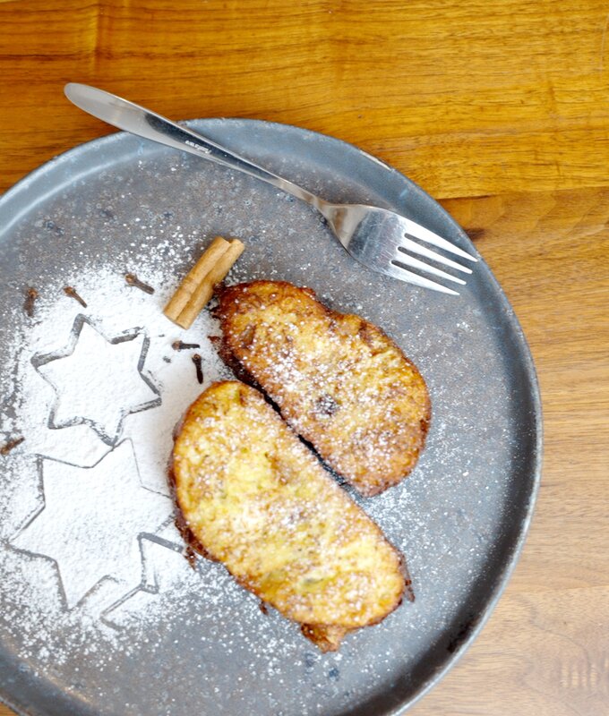 Auf einem grauen Teller liegen zwei goldbraune, mit Puderzucker bestäubte Gebäckstücke. Neben ihnen sind Sterne aus Puderzucker dekoriert. Vor dem Hintergrund einer Holzoberfläche lässt sich eine gabelähnliche Besteckposition erkennen. | © Urlaub am Bauernhof / Daniel Gollner