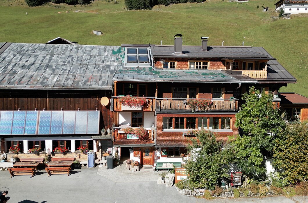Traditionelles Berghotel mit hölzerner Fassade und Balkonen, das von Bergwiesen umgeben ist. Große, verglaste Außenterrasse lädt zum Verweilen ein. Insgesamt ein rustikaler, gemütlicher Charakter des Gebäudes. | © Urlaub am Bauernhof / Daniel Gollner
