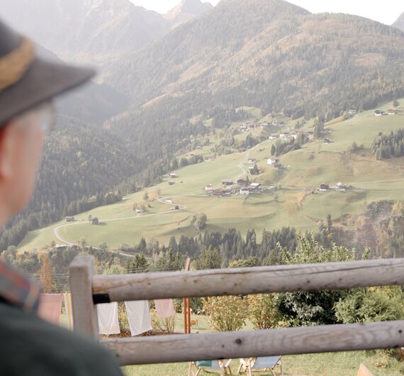 Weites Bergpanorama mit bewaldeten Hängen, durchzogen von Bergwiesen und verstreuten Häusern. Im Vordergrund ein Holzzaun, der den Blick auf die Landschaft rahmt. | © Urlaub am Bauernhof / Daniel Gollner