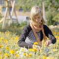 Eine junge Frau in einem blühenden Blumenfeld, die sorgfältig Blumen pflückt. Sie trägt einen dunklen Pullover und einen Schal und scheint sich in der Natur wohlzufühlen. | © Urlaub am Bauernhof / Daniel Gollner