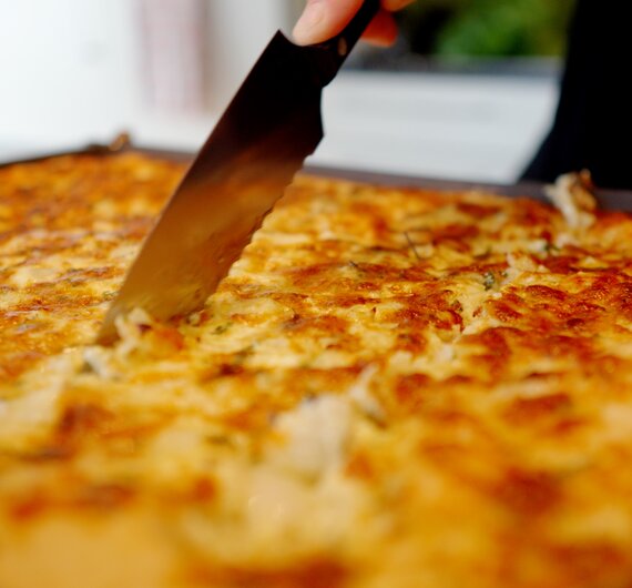 Eine leckere, goldbraune Tortilla mit geschmolzenem Käse, die gerade mit einem Messer zerteilt wird. | © Urlaub am Bauernhof / Daniel Gollner