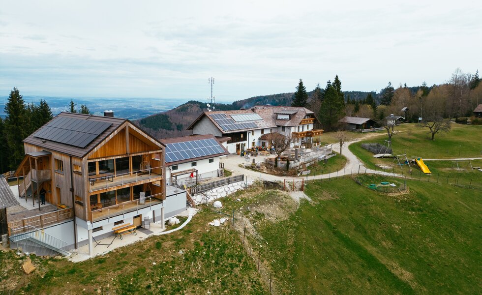 Ein Bergort mit Holzhäusern, Sonnenkollektoren und Freizeitanlagen inmitten einer grünen Landschaft. Kleine Wege und Treppen führen durch die Anlage.