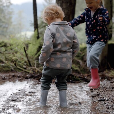 Zwei Kinder spielen bei Regen im Wald, der eine trägt einen gemusterten Pullover, der andere hat Gummistiefel an. | © Urlaub am Bauernhof / Daniel Gollner