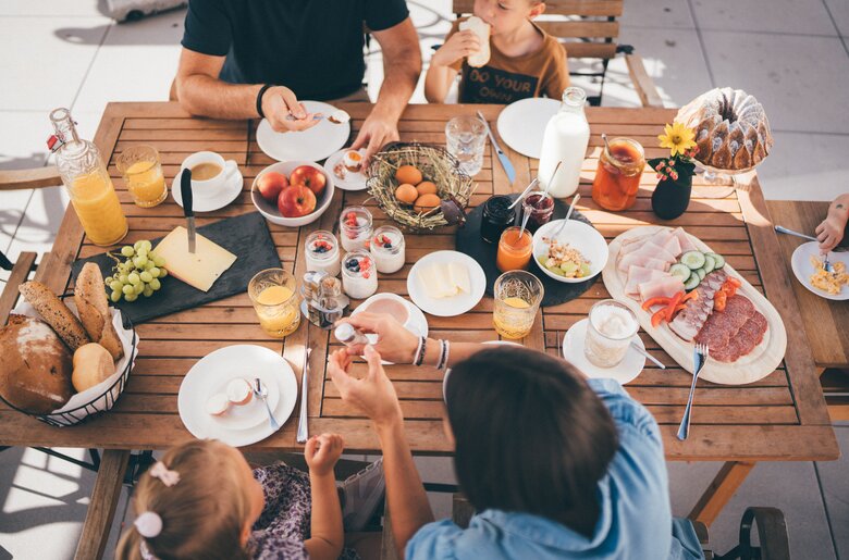 Gemütliches Frühstück mit verschiedenen Speisen und Getränken auf Holztisch. Mehrere Personen sitzen gemeinsam und genießen die Mahlzeit in entspannter Atmosphäre. | © Urlaub am Bauernhof / Daniel Gollner