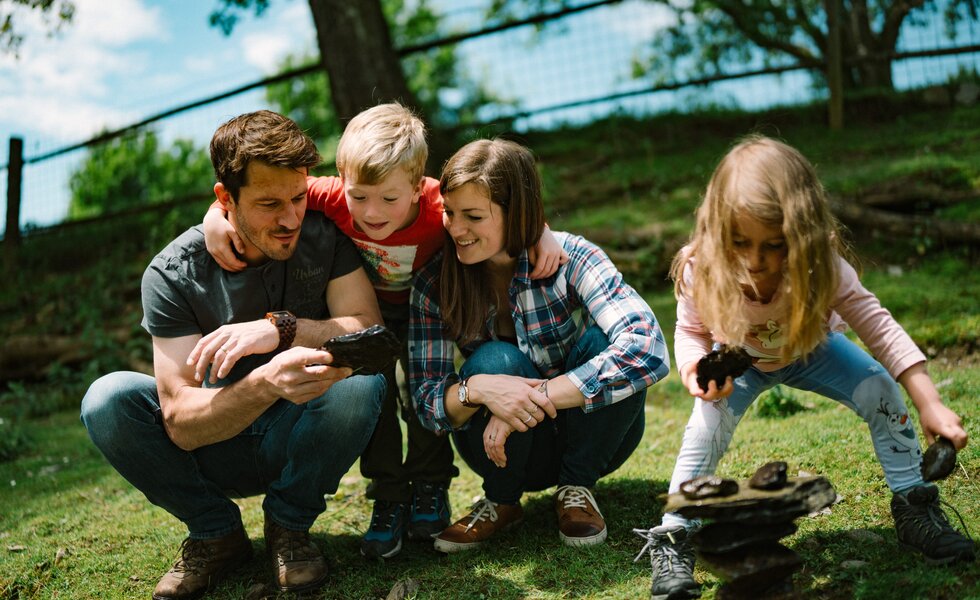 Vier Personen, zwei Erwachsene und zwei Kinder, sitzen in einem Garten auf dem Rasen und betrachten etwas gemeinsam. Die Atmosphäre ist entspannt und fröhlich. | © Urlaub am Bauernhof / Daniel Gollner 