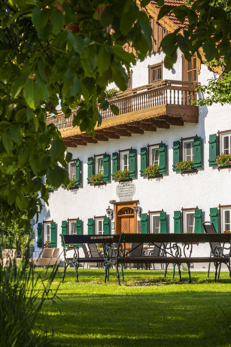 Ein malerisches historisches Gebäude mit Balkonen, Fensterläden und Blumenkästen, umgeben von schattigem Laubwerk und einem gepflegten Garten mit Sitzgelegenheiten. Idyllische ländliche Atmosphäre, die zu Ruhe und Entspannung einlädt. | © Urlaub am Bauernhof Österreich / Bernd Suppan