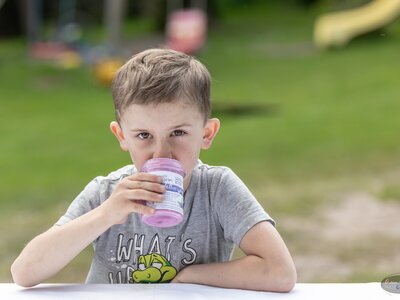 Bub trinkt Heidelbeerjoghurt | © Bio-Bergbauernhof Weger Bub sitzt auf einer Bank und genießt sein Heidelbeerjoghurt | © Bio-Bergbauernhof Weger