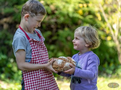 Zwei Kinder mit Brotlaib | © Bio-Bergbauernhof Weger Zwei Kinder schauen sich an und geben sich einen Laib Brot | © Bio-Bergbauernhof Weger