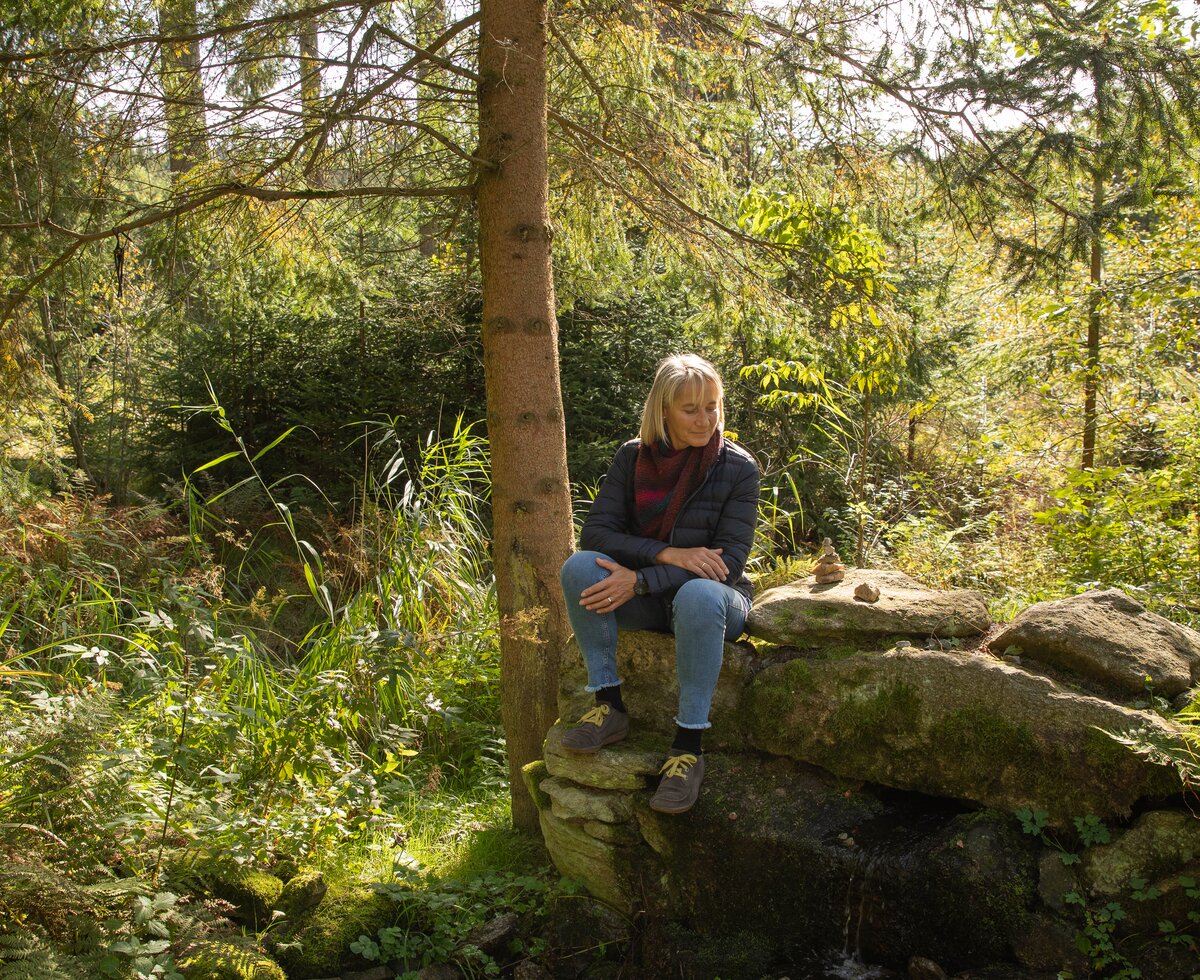 Frau sitzt auf Stein im Wald | © Urlaub am Bauernhof / Punkt und Komma Frau sitzt auf einem Stein im Wald | © Urlaub am Bauernhof / Punkt und Komma