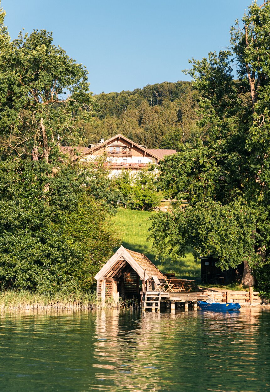 Ruhige Seelandschaft mit Bootsanleger und malerischem Holzhaus in einer waldigen Umgebung. Idyllische Stimmung vermittelt Erholung und Entspannung. | © Urlaub am Bauernhof / Punkt und Komma