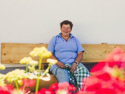 Host sits on the house bench | © Farmholidays in SalzburgerLand / Matthias Gruber Host Karin Pöllmann from the Stallerbauer in Ried am Wolfgangsee sits on the house bench. | © Farmholidays in SalzburgerLand / Matthias Gruber