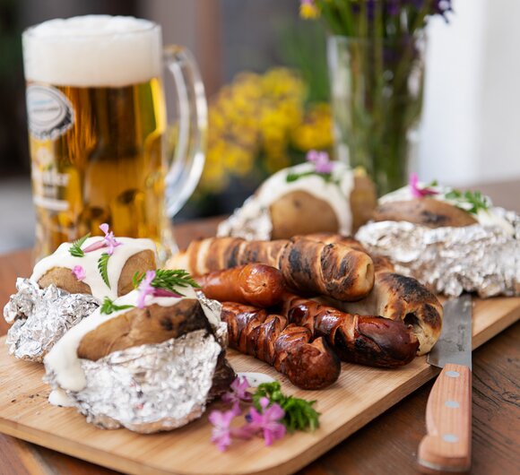 Gegrillte Würstchen, gegrilltes Stockbrot, Kartoffel  und ein Glas Bier im Hintergrund | © Carlettophotography/Urlaub am Bauernhof SalzburgerLand