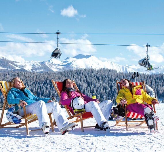 Drei Skifahrerinnen genießen die Sonne in Sonnenliegen auf der Piste, im Hintergrund Sessellift, Salzburger Sportwelt | © Salzburger Sportwelt 
