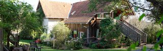 Ein altes Nebengebäude am Bauernhof, das als Ferienhaus liebevoll renoviert wurde, Aufgang zum Eingang ist eine Holzstiege, davor befindet sich eine gepflegte Wiese mit Sitzmöbeln aus Holz | © Urlaub am Bauernhof Steiermark / Daniel Gollner