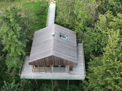 Baumhaus aus Holz mit Terrasse runderhum, fotografiert aus Vogelperspektive, umgeben von grünen Bäumen | © Familie Fröhlich-Graz / Nebel