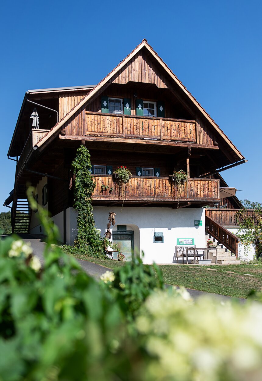 Ein großes Bauernhaus aus Holz mit Blumen im Vordergrund | © Urlaub am Bauernhof / Carletto Ferrari-Brunnenfeld 