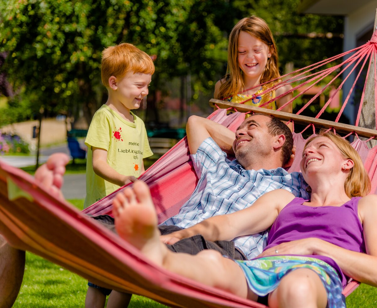 Eltern mit Kindern in der Hängematte, Oststeiermark, Steiermark | © Urlaub am Bauernhof Steiermark / Wolfgang Spekner Eltern liegen in der Hängematte und Kinder stehen daneben, Oststeiermark, Steiermark | © Urlaub am Bauernhof Steiermark / Wolfgang Spekner