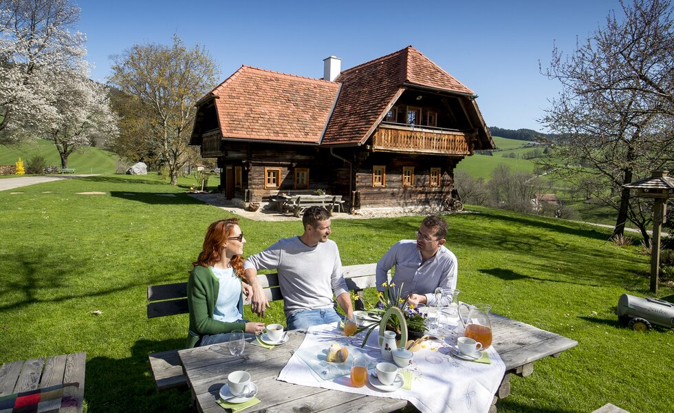 Der Bauer sitzt mit seinen Gästen beim österlich gedeckten Kaffeetisch im Freien, Steiermark | © Urlaub am Bauernhof Steiermark / Tom Lamm