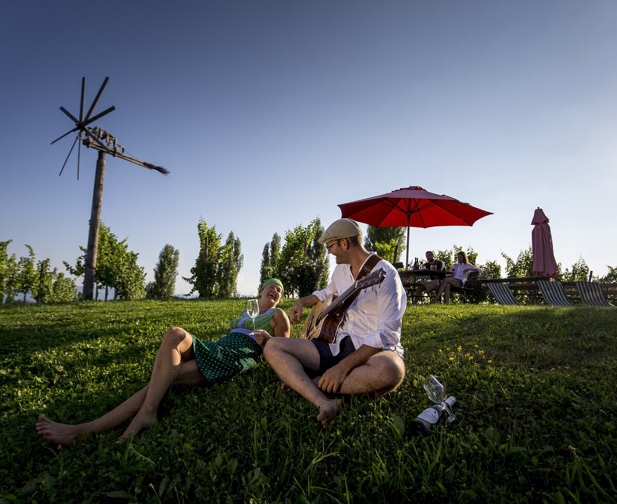 Ein Paar sitzt in der Wiese im Weingarten, Süd-West-Steiermark, Steiermark | © Süd-West-Steiermark / ikarus.cc Ein Paar sitzt mit Wein und Gitarre in der Wiese im Weingarten, Süd-West-Steiermark, Steiermark | © Süd-West-Steiermark / ikarus.cc