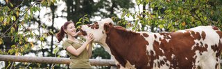 Eine Kuh schleckt eine junge Frau im Gesicht ab, Forstbauer, Steiermark | © Urlaub am Bauernhof / Punkt & Komma