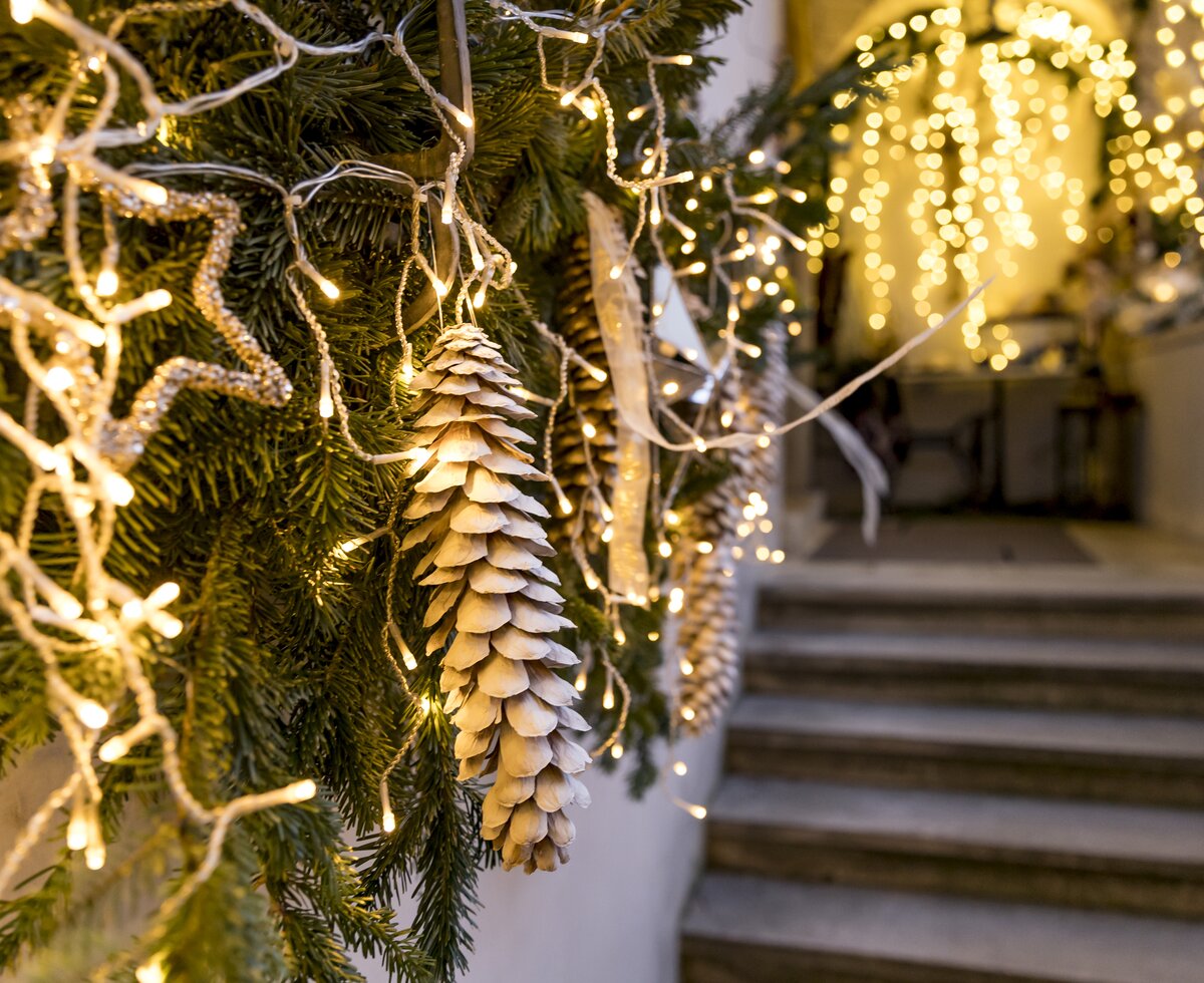 Ein beleuchteter Weihnachtsbaum mit goldenen Zapfen und Lichterketten, vor einer Treppe und einer Fassade mit Lichterketten in einer festlichen Umgebung.