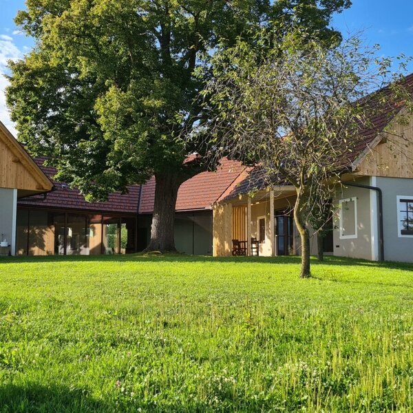 Außenansicht des revitalisierten Dreikanthofs mit großer Grünfläche, alten Bäumen und Ansicht der umliegenden Weingärten.