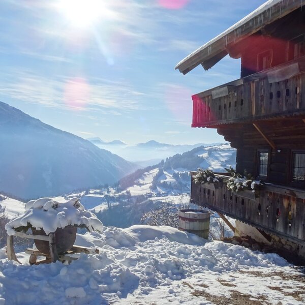 The Alpine Hut featuring a wooden balcony with a view of the snowy mountain landscape under a bright sun.