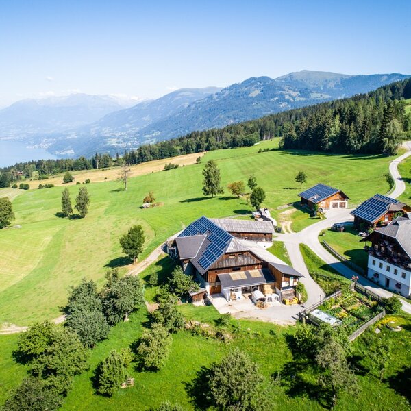 The Farm House property, featuring multiple buildings with solar panels, is set within green hills and overlooks a lake and mountains.