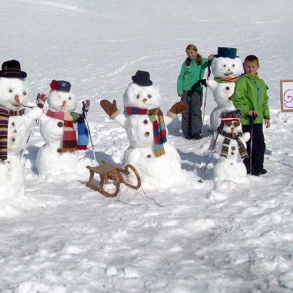 Several decorated snowmen and children in the snow at the Farm House.